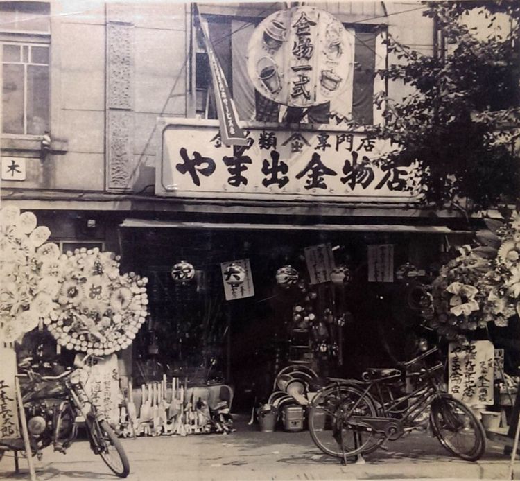 やま出金物店は、現在の京都市下京区大宮七条西入る の北側（現在のみずほ銀行の付近）にありました。梅次郎の好みにより夜中まで煌々とネオンが輝く非常に派手な店構えだったとのことです。
